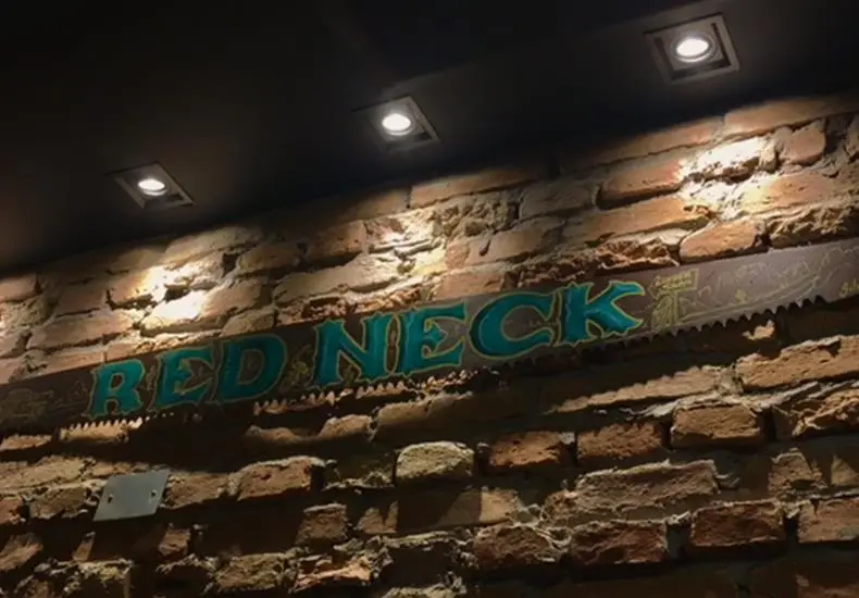 Letreiro Red Neck pintado num serrote antigo sobre a parede de tijolos